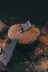 Chocolate bar pieces with cocoa powder on dark background, cope space