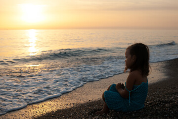 Fototapeta na wymiar child a girl in a blue knitted dress by the sea walks and watches the sunset. Turkey