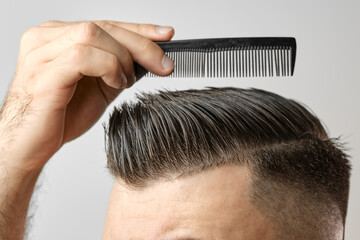 Naklejka premium Close up young man combing his hair with a plastic comb. Styling hair after barbershop. 