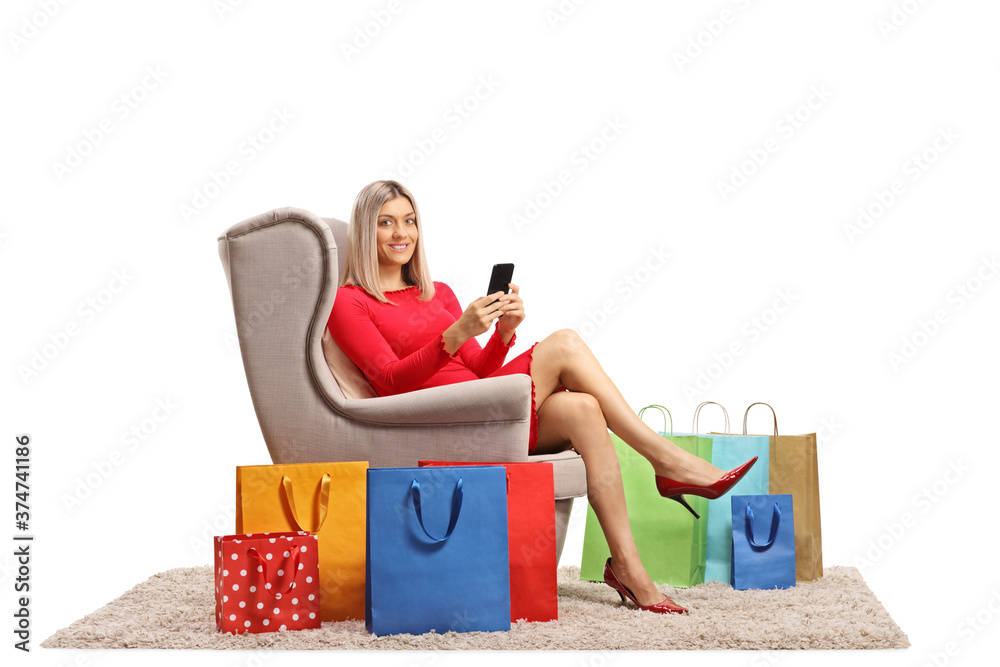 Wall mural young woman in an armchair with a mobile phone and shopping bags