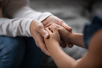 Close up compassionate young foster parent holding hands of little kid girl, giving psychological...