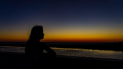 Fototapeta premium Silhouette of a young woman with fluttering hair against the background of a bright sunset
