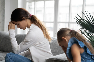 Frustrated young mixed race woman touching forehead, feeling stressed after family conflict with little naughty child daughter, avoid talking to each other, suffering from headache or depression.