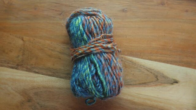 A skein of colorful yarn on a spinning wooden table top.  Close up shot of multicolored fiber ready to be crafted into a garment.