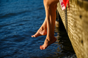 Female legs hanging off of a dock over water with toes touching water