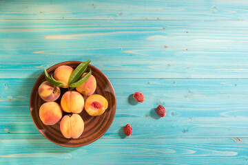 Several ripe velvety juicy and beautiful peaches with leaves lie in a plate on a blue wooden table....