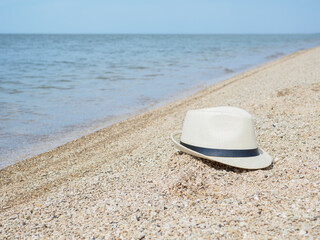 Fototapeta na wymiar A white straw hat lies on the sand by the water. Sea beach on a summer sunny day. Sea vacation concept. Copy space. High quality photo