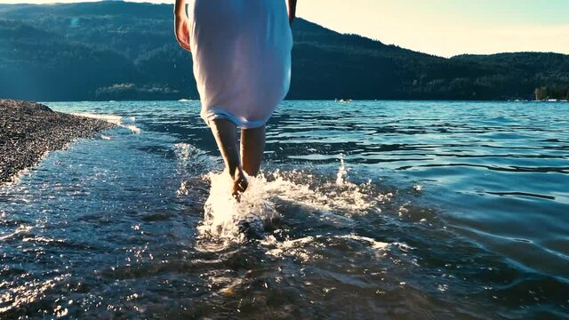 Summer scene of the Cultus Lake with a woman in the foreground walking in the water in slow motion. Chilliwack, British Columbia, Canada