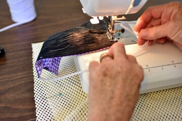 Close-up of woman's hands sewing handmade masks for the family that are required to wear in public during pandemic