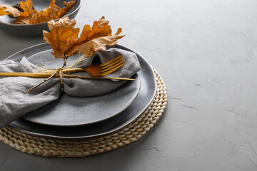 Elegant table setting with autumn oak leaves and golden cutlery on grey background. Close up.