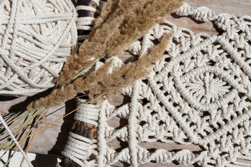 Fragment of macrame product made of natural cotton rope of milk color on a wooden board