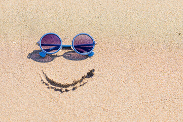 Fototapeta na wymiar Sunglasses and a painted smile on a sandy beach. Travel concept