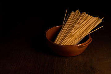 Pasta in a brown bowl on a dark wood table with moody lighting.