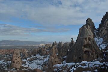 Fototapeta na wymiar Another hilltop view of the fairy chimneys and historical caves in Cappadocia. Cappadocia from the top on a snowy winter day. Settlements beyond the fairy chimneys. The path leading up the hill.