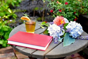 Pretty floral bouquet of fresh cut flowers on outdoor wooden table with refreshing glass of iced...