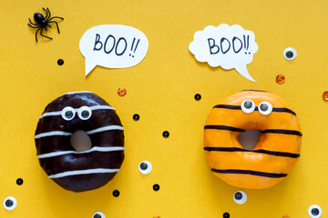 Happy halloween holiday concept. Funny food for kids - scared donuts bright yellow background with black spider and eyes. Halloween party greeting card. Spelling word Boo Flat lay, top view, overhead