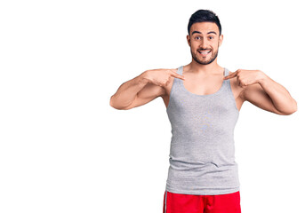 Young handsome man wearing swimwear and sleeveless t-shirt looking confident with smile on face,...