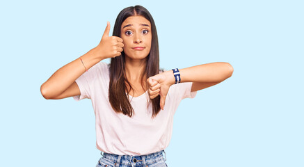 Fototapeta premium Young hispanic woman wearing casual white tshirt doing thumbs up and down, disagreement and agreement expression. crazy conflict