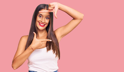 Fototapeta premium Young hispanic woman wearing casual clothes smiling making frame with hands and fingers with happy face. creativity and photography concept.
