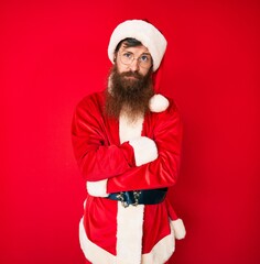 Handsome young red head man with long beard wearing santa claus costume skeptic and nervous, disapproving expression on face with crossed arms. negative person.
