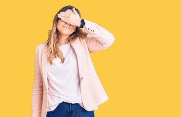 Young caucasian woman wearing business clothes covering eyes with hand, looking serious and sad. sightless, hiding and rejection concept