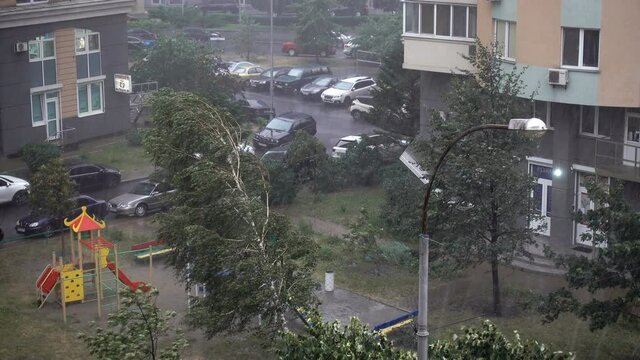 4K view of rain and wind in a city courtyard. Playground downpour and swaying trees