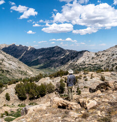 Person, hiker, man, looking at a view from a high pass down into a valley and mountains, with rocks, blue sky puffy clouds, Liberty Pass, Ruby Mountain Wilderness, Nevada