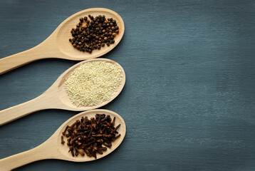 Various spices on wooden spoons on a dark background. Selective focus. Space for text. Black pepper, cloves and white sesame on wooden spoons. Kitchen herbs