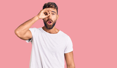 Fototapeta premium Young hispanic man wearing casual white tshirt doing ok gesture shocked with surprised face, eye looking through fingers. unbelieving expression.