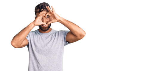 Young hispanic man wearing casual clothes doing heart shape with hand and fingers smiling looking through sign