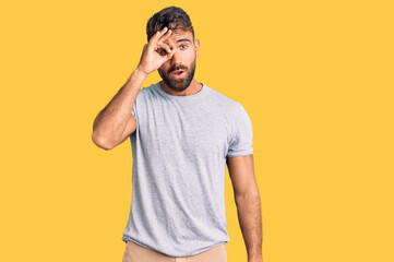 Fototapeta premium Young hispanic man wearing casual clothes doing ok gesture shocked with surprised face, eye looking through fingers. unbelieving expression.