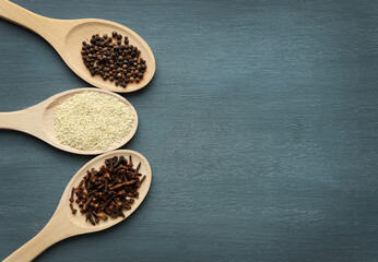 Black pepper, cloves and white sesame on wooden spoons lie beautifully on a dark wooden background. Selective focus. Space for text. Various spices