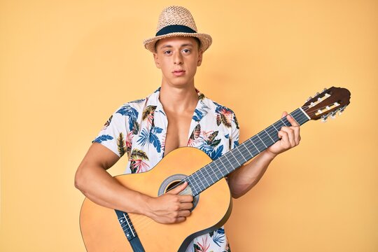Young hispanic boy wearing summer style playing classical guitar relaxed with serious expression on face. simple and natural looking at the camera.
