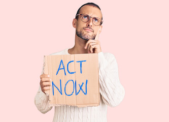 Young handsome man holding act now banner serious face thinking about question with hand on chin,...