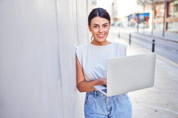 Beautiful young woman wearing fashionable clothes walking down the street and working using computer laptop