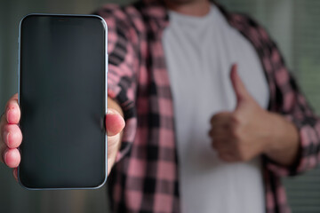A man in a pink plaid shirt with a cell phone in his hand. White T-shirt.