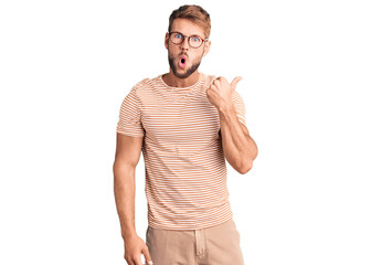 Young caucasian man wearing casual clothes and glasses surprised pointing with hand finger to the side, open mouth amazed expression.