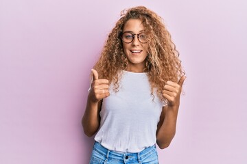 Beautiful caucasian teenager girl wearing white t-shirt over pink background success sign doing positive gesture with hand, thumbs up smiling and happy. cheerful expression and winner gesture.