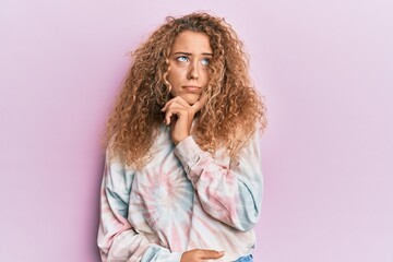 Beautiful caucasian teenager girl wearing casual tie dye sweatshirt serious face thinking about question with hand on chin, thoughtful about confusing idea