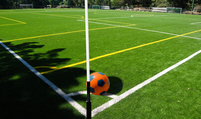 Campo de treinos de futebol, vista de um canto para o centro do campo com uma bola laranja e azul