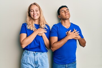 Young interracial couple wearing casual clothes smiling with hands on chest with closed eyes and grateful gesture on face. health concept.