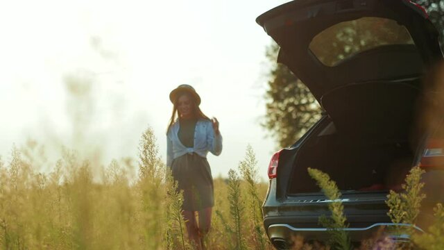 Charming young woman with hat walking near her car enjoying sunset view in field expression design sun warm nature business holidays vacations young slow motion