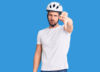 Young handsome man wearing bike helmet looking unhappy and angry showing rejection and negative with thumbs down gesture. bad expression.