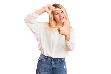 Obraz na płótnie Canvas Young beautiful blonde woman wearing casual shirt smiling making frame with hands and fingers with happy face. creativity and photography concept.