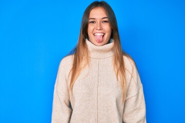 Fototapeta premium Beautiful caucasian woman wearing wool winter sweater sticking tongue out happy with funny expression. emotion concept.
