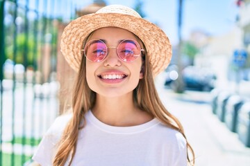 Young beautiful blonde caucasian woman smiling happy outdoors on a sunny day wearing summer hat and pink sunglasses