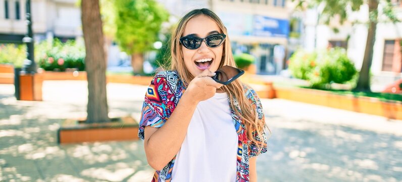 Young beautiful blonde caucasian woman smiling happy outdoors on a sunny day using smartphone