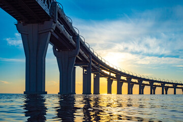 Fototapeta premium Road bridge at sunset. Two-level bridge over the water. Highway over the Bay. The highway passes over the river. A long bridge over the water and the setting sun.