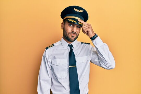Handsome hispanic man wearing airplane pilot uniform pointing unhappy to pimple on forehead, ugly infection of blackhead. acne and skin problem