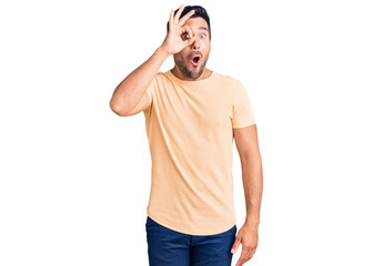 Fototapeta premium Young hispanic man wearing casual clothes doing ok gesture shocked with surprised face, eye looking through fingers. unbelieving expression.
